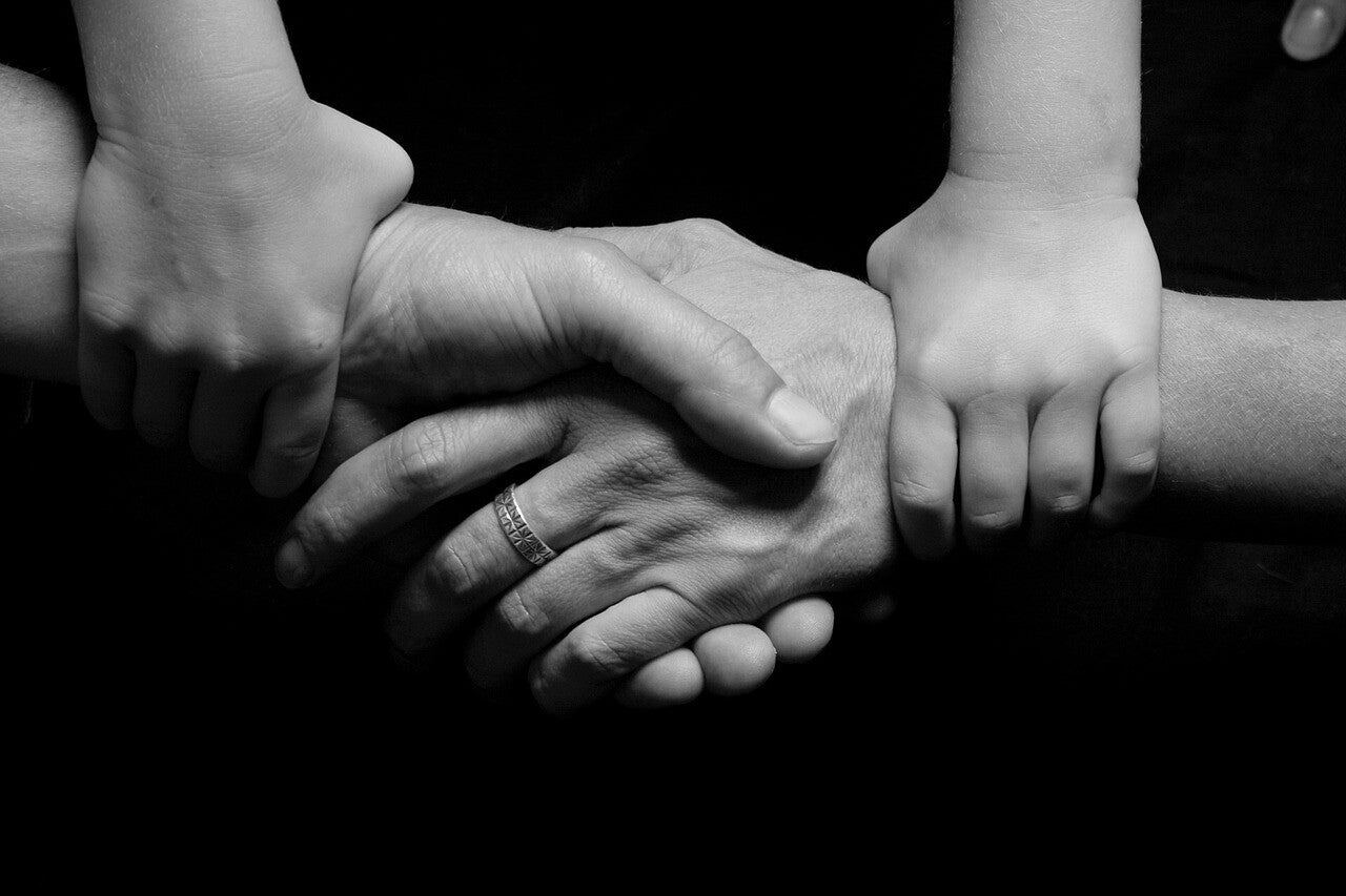 Black-and-white photograph of the hands of a grandparent, a parent and a child resting on one another